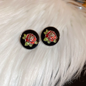 Close-up of black enamel round stud earrings with red rose pattern on white fur background