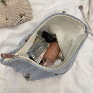 Top view of a blue corduroy makeup bag with cute bear embroidery on white fabric