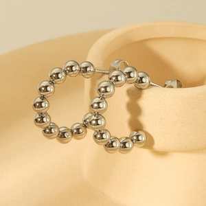 Macro shot of silver beaded hoop earrings hanging on a minimalist ceramic vessel