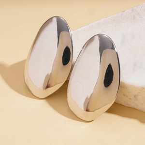 Detailed close-up of polished silver teardrop earrings on a white stone background