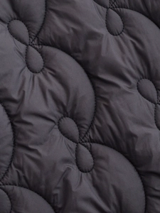 Macro shot of dark grey quilted fabric with wavy stitching on winter jacket coat