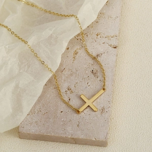 Polished gold stainless steel horizontal cross necklace on a natural stone background