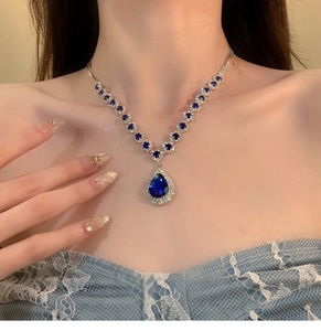 Detail of a luxury silver-toned necklace with blue teardrop sapphire on a model