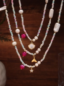 Detail of layered beaded necklace with pastel pearls, shell, whale tail, and star charms