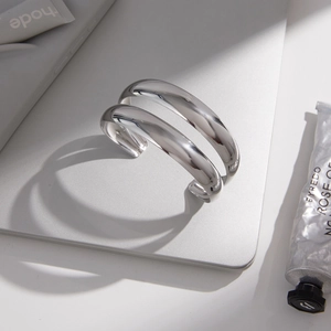 Polished silver stainless steel cuff bracelet shown at a 45-degree angle on a gray surface