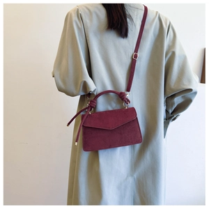 Detail of burgundy suede crossbody bag with envelope flap and matching shoulder strap