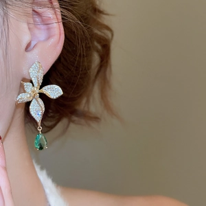 Detail view of a 18k gold floral earring with a pear-cut green gemstone on a model