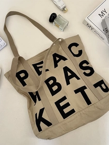 Minimalist beige canvas tote bag with black Peace Basket lettering in a flat lay setup