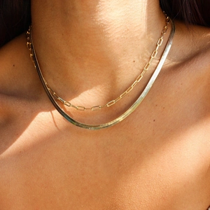 Detail of layered gold herringbone and paperclip chain necklaces on model's neck
