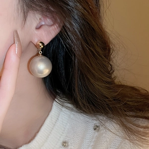Gros plan d'un mannequin portant de longues boucles d'oreilles dorées à perle blanche ronde