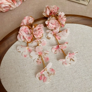 Detail of pink chiffon flower tassel earrings on a textured linen display tray