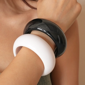 Close-up of thick geometric resin bangles in glossy black and white on a model wrist