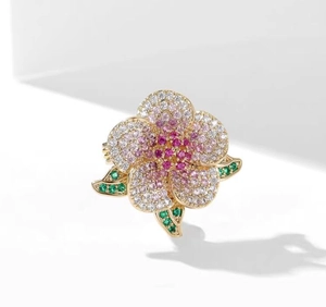Macro detail of camellia brooch with pink and white pavé crystals and green leaves