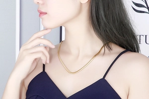 Gros plan d'un collier chaîne serpent plate dorée minimaliste sur le cou