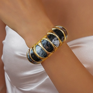 Detail of chunky gold bracelet with black and white marbled resin inlay on model
