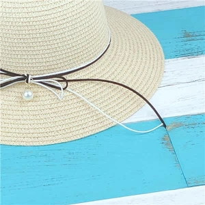 Detail of straw hat with decorative bow and elegant pearl charm on wood background