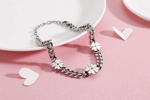 Detail view of silver stainless steel clover bracelet with mini charms on white plate