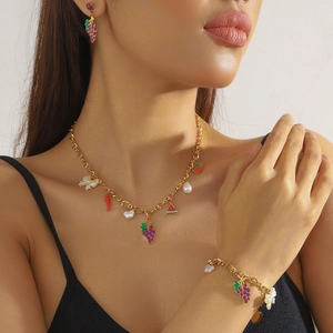 Modeschmuck-Set mit goldenen Obst-Emaille-Anhängern und Perlen an einem weiblichen Model