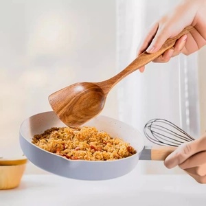 Natural teak wood spatula with long handle scooping fried rice from a cooking pan