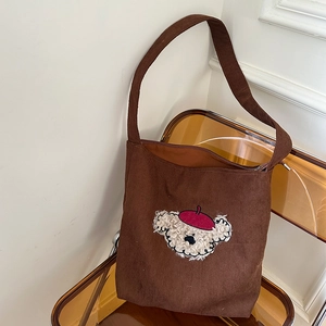 Detail of brown corduroy tote bag featuring a cute 3D teddy bear patch on a chair