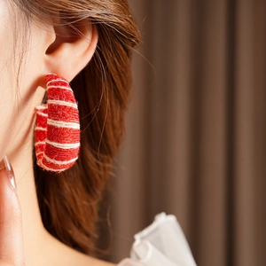 Close-up of red and white woven fabric C-shaped earrings worn by a female model
