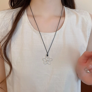 Gros plan d'un pendentif fleur argenté évidé sur un cordon de cire noir porté par un mannequin