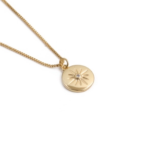 Détail du pendentif pièce soleil doré avec cristal sur une fine chaîne box