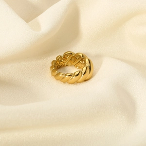 Detailed view of the twisted 18K gold-plated titanium steel ring on elegant cream fabric
