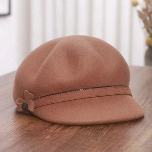 Brown wool newsboy hat with pearl strap and bow detail on a vintage wooden surface
