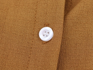 Gros plan sur le tissu texturé marron et le bouton blanc de la robe d'été longue