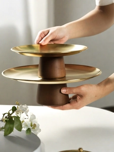 Close-up of model holding a two-tier gold metal and wood snack tray for afternoon tea