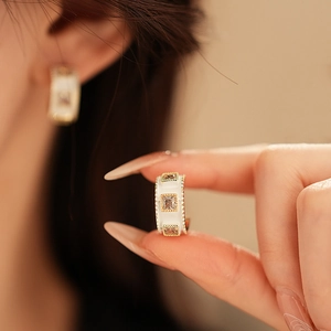 Detail of C-shaped gold-plated earring with white enamel and square zircon gemstone