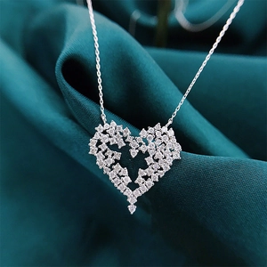 Close-up of silver hollow heart pendant with sparkling crystals on green silk