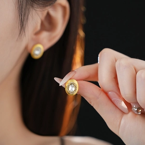 Close-up of matte gold oval stud earrings with center crystal and sparkling diamond halo