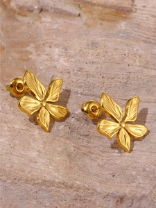 Close-up of golden five-petal flower earrings with fine textures on a natural stone surface