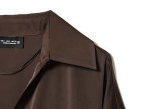 Détail du col d'une chemise en satin marron foncé avec étiquette S et texture de tissu