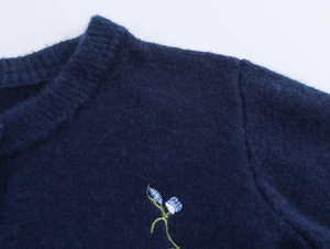 Detail of floral embroidery on a navy blue round-neck knit cardigan with soft texture
