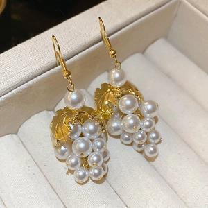 Macro detail of French grape bunch earrings with lustrous pearls and golden leaf texture