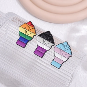 Detalle de tres pines de esmalte con forma de puño y colores LGBTQ+ sobre vidrio texturizado