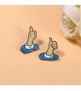 Detailed view of two cartoon thumbs up enamel brooches on vibrant orange background