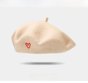 Close-up of beige wool beret featuring a delicate red heart embroidery detail