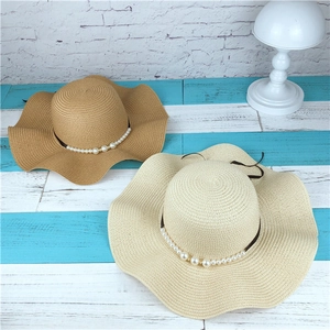 Detail of wavy brim straw hats with pearls and black ribbon on a striped background