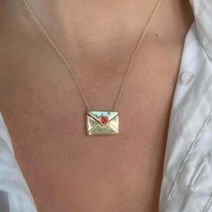 Collier pendentif enveloppe doré avec cœur en zircon rouge porté sur chemise blanche