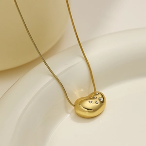 Detail of gold bean pendant necklace with micro-pave crystals on a sleek snake chain
