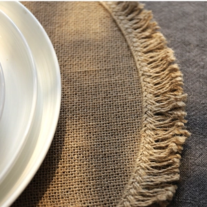 Round minimalist jute placemat with fringe edge, natural linen texture for dining table