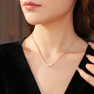Detail of gold tennis necklace with graduated round clear zircon stones on a female model