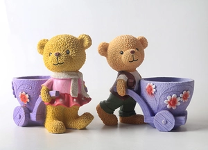 Dettaglio di fioriere in resina a forma di orsetti gialli con carrelli viola e fiori