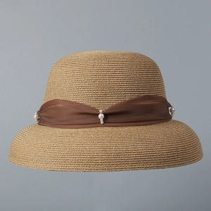 Dettaglio di un cappello di paglia estivo con nastro marrone e decorazioni di perle