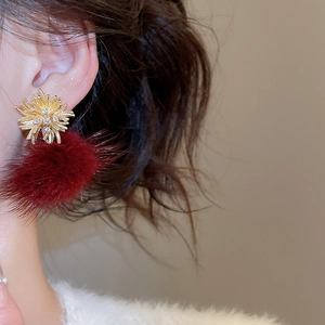 Close-up of golden rhinestone firework studs with plush deep red pompom drop earrings
