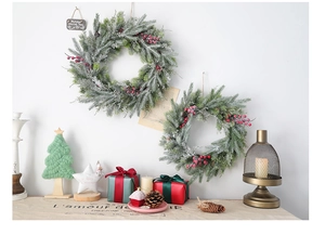 Détail de couronne de Noël enneigée avec baies rouges et pommes de pin sur mur blanc